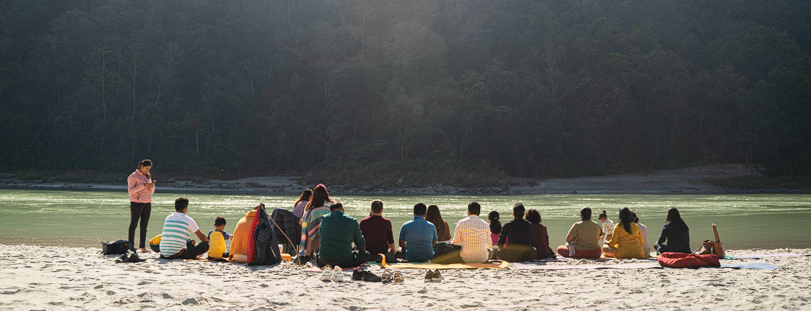 Retreat participants seated in a circle by a river at sunrise